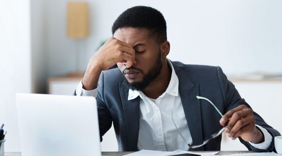 man rubbing his eyes in front of computer