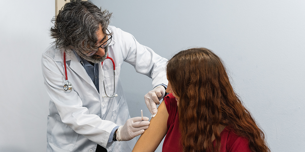 senior doctor putting band aid on arm of patient after flu vaccination