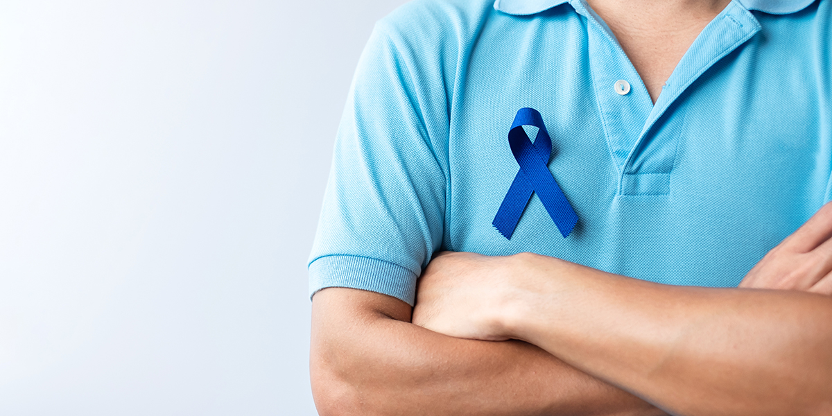 man standing with arms crossed wearing blue ribbon for Colorectal Cancer Awareness month