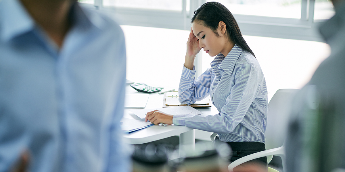 woman staring at documents at desk look stressed, people blurred in front of her